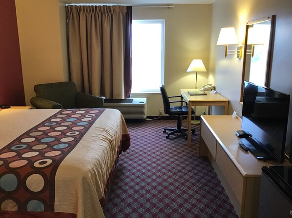 A hotel room with a bed, desk, chair, television, and a window with curtains.