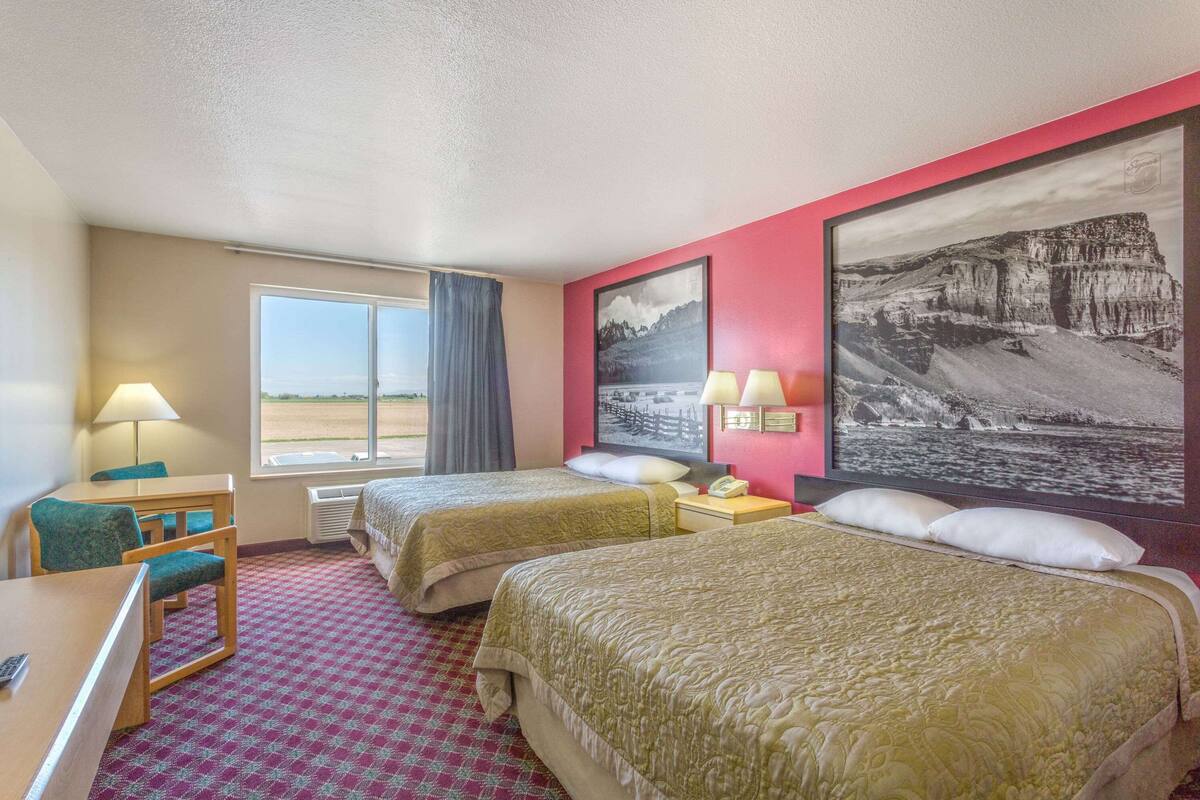 Een hotelkamer met twee bedden, een bureau met stoel, een raam met uitzicht en twee lampen.