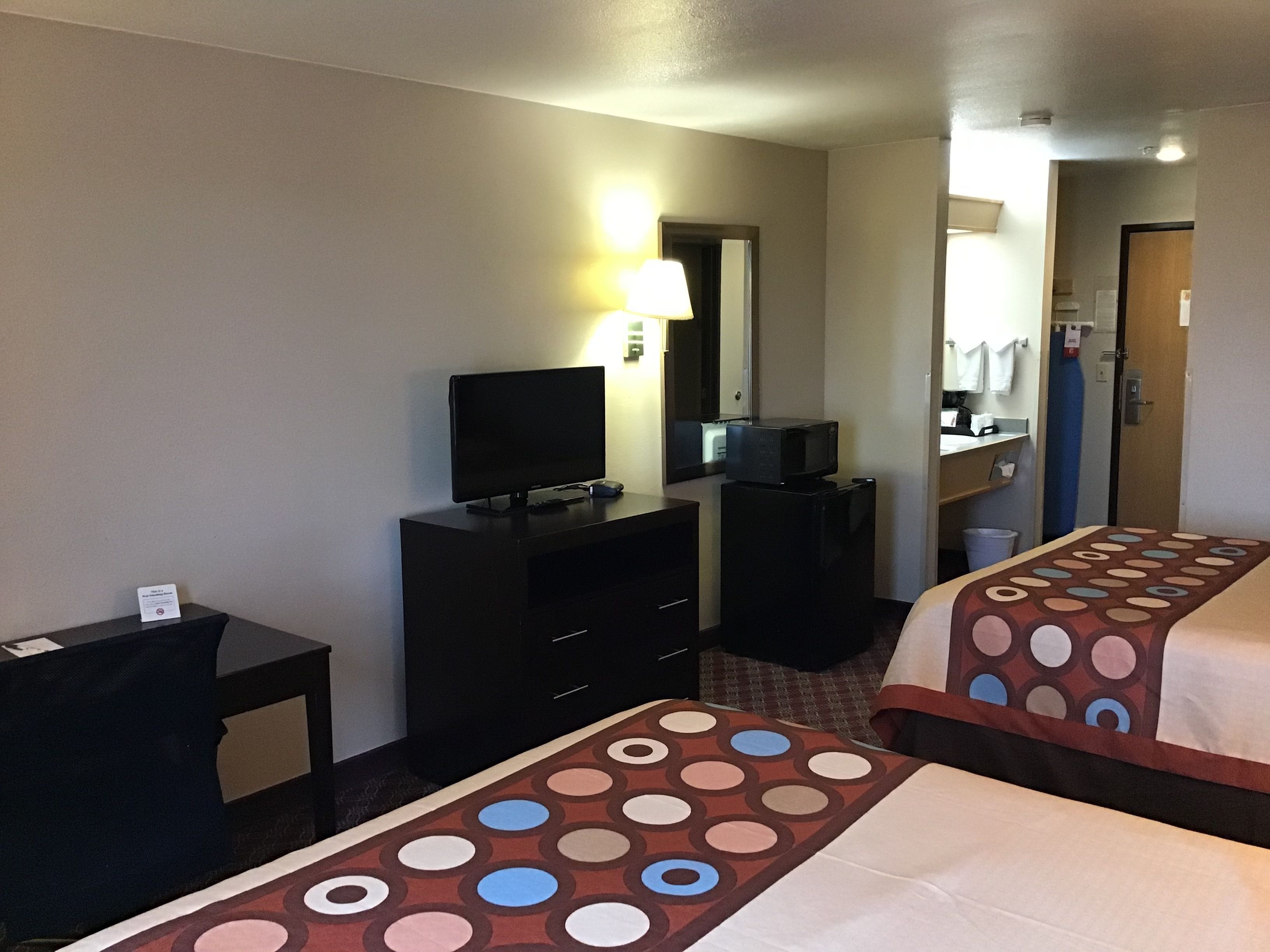 A hotel room with two beds, a desk, a dresser, a television, and a mirror.