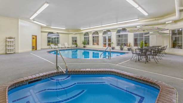 An indoor swimming pool with clear blue water, surrounded by lounge chairs and a table with chairs.