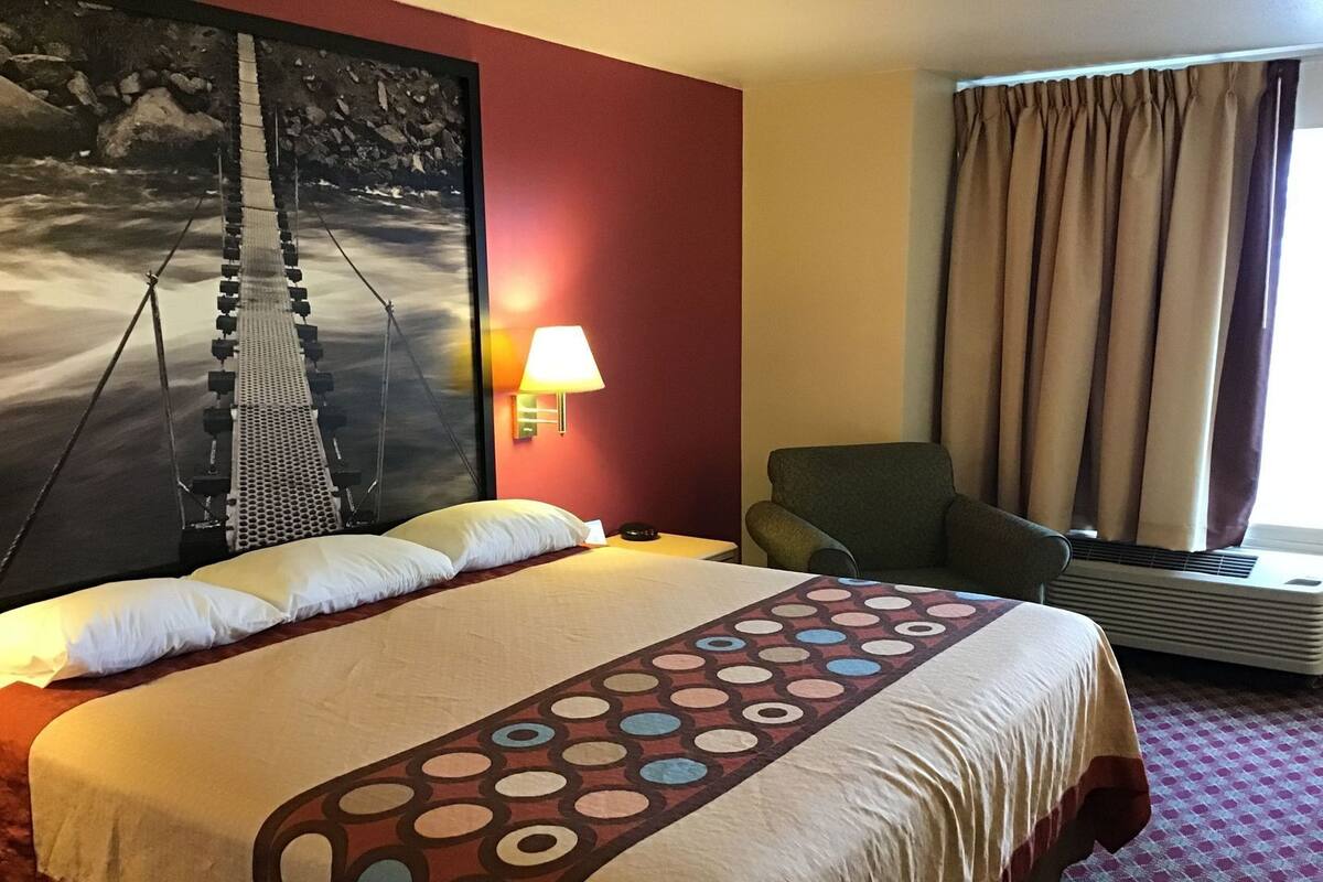Een hotelkamer met een groot bed, een stoel, een wandlamp en een raam met gordijnen.