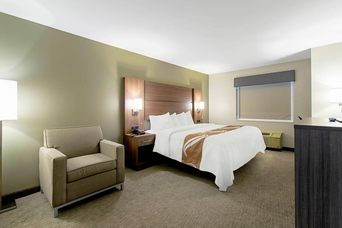 A hotel room with a bed, a chair, a nightstand, and a desk.