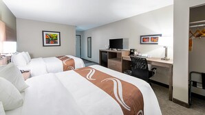 Habitación de hotel con dos camas, un escritorio, una silla, un televisor y obras de arte en las paredes.