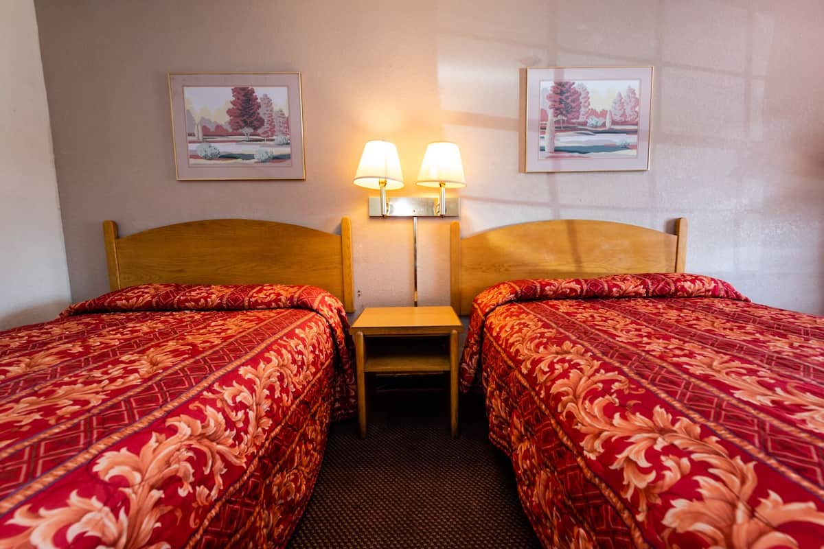 A hotel room with two beds, a nightstand, and two wall-mounted lamps.