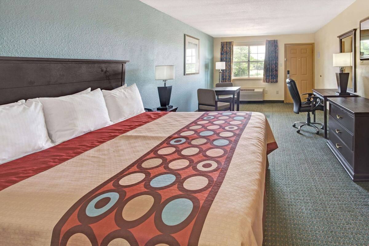 Une chambre d’hôtel avec un grand lit, un bureau, une chaise, une commode et une fenêtre avec des rideaux.