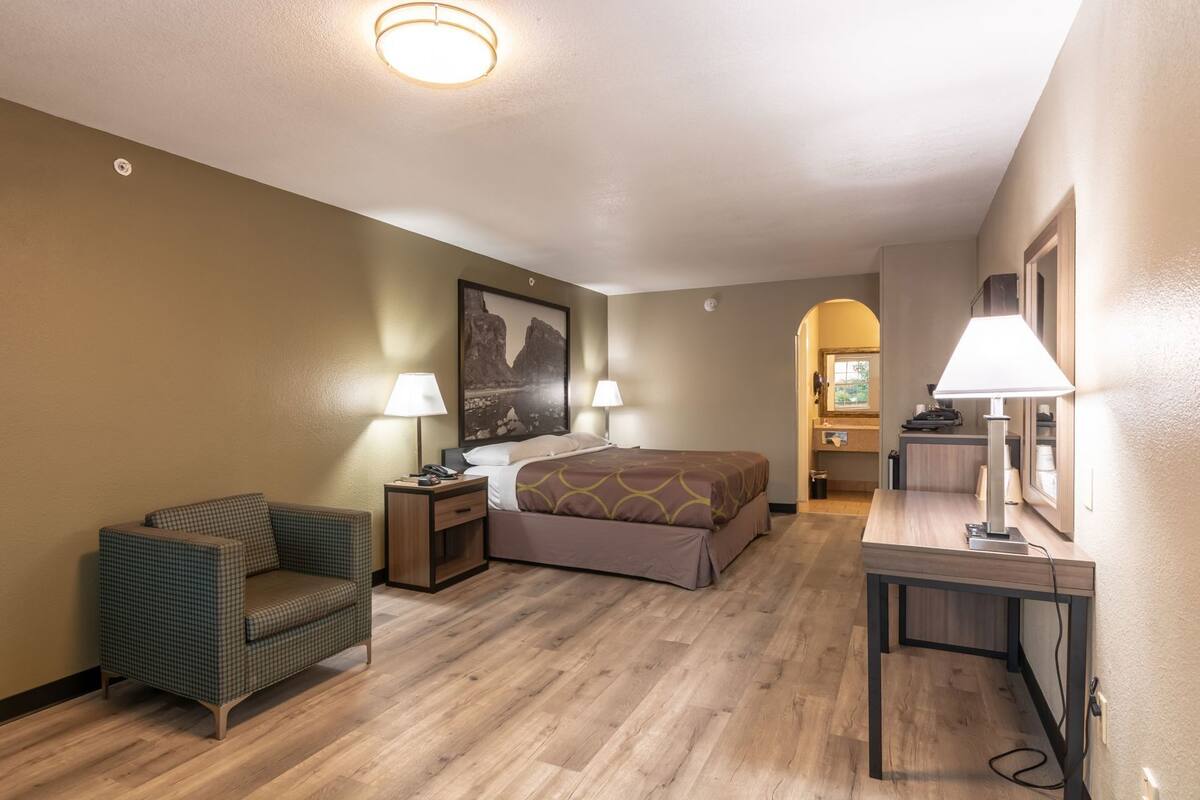 Une chambre d’hôtel avec un lit, une chaise, un bureau et une salle de bain visible à travers une arche.