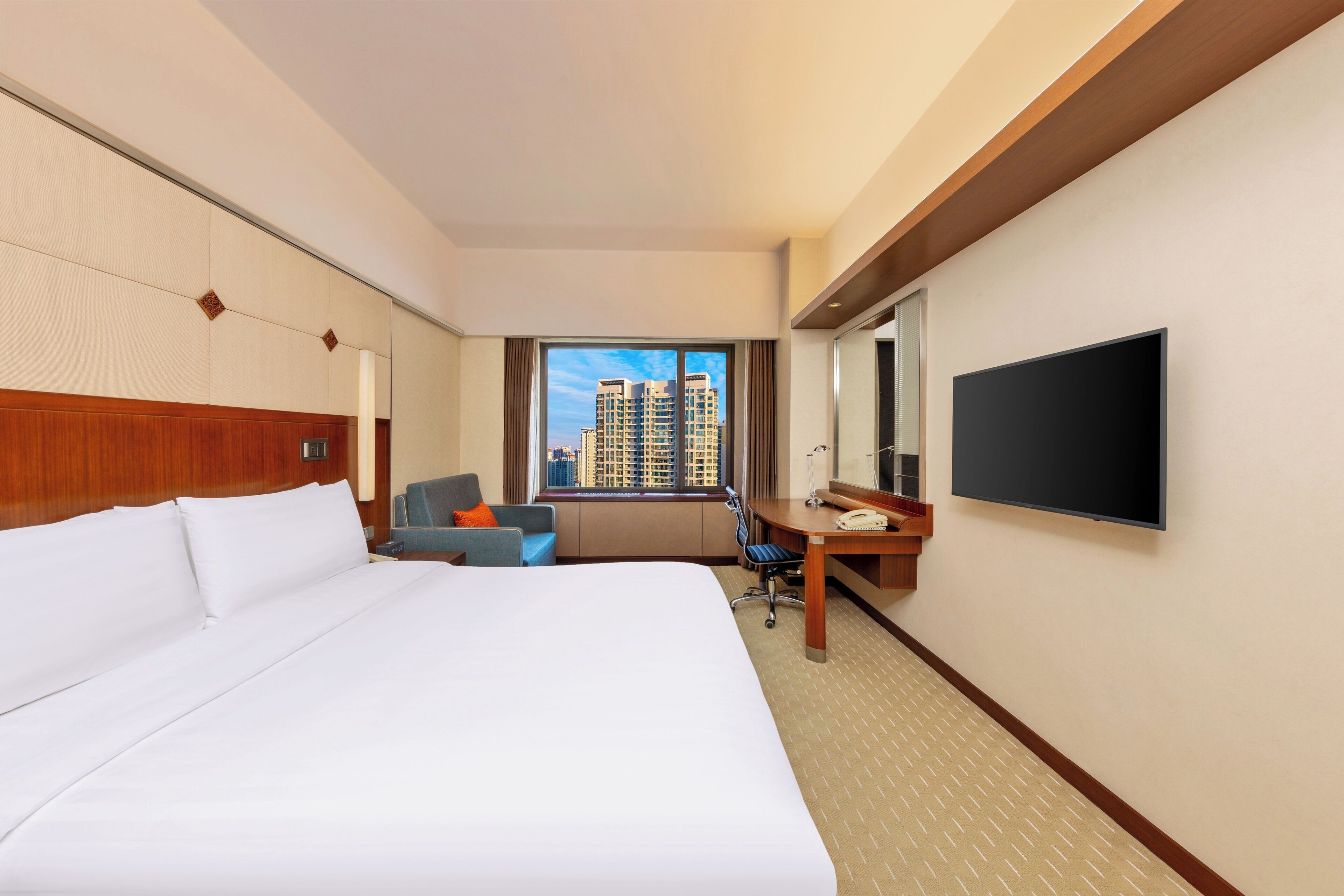 A hotel room with a large bed, a desk with a chair, a television, and a window with a city view.