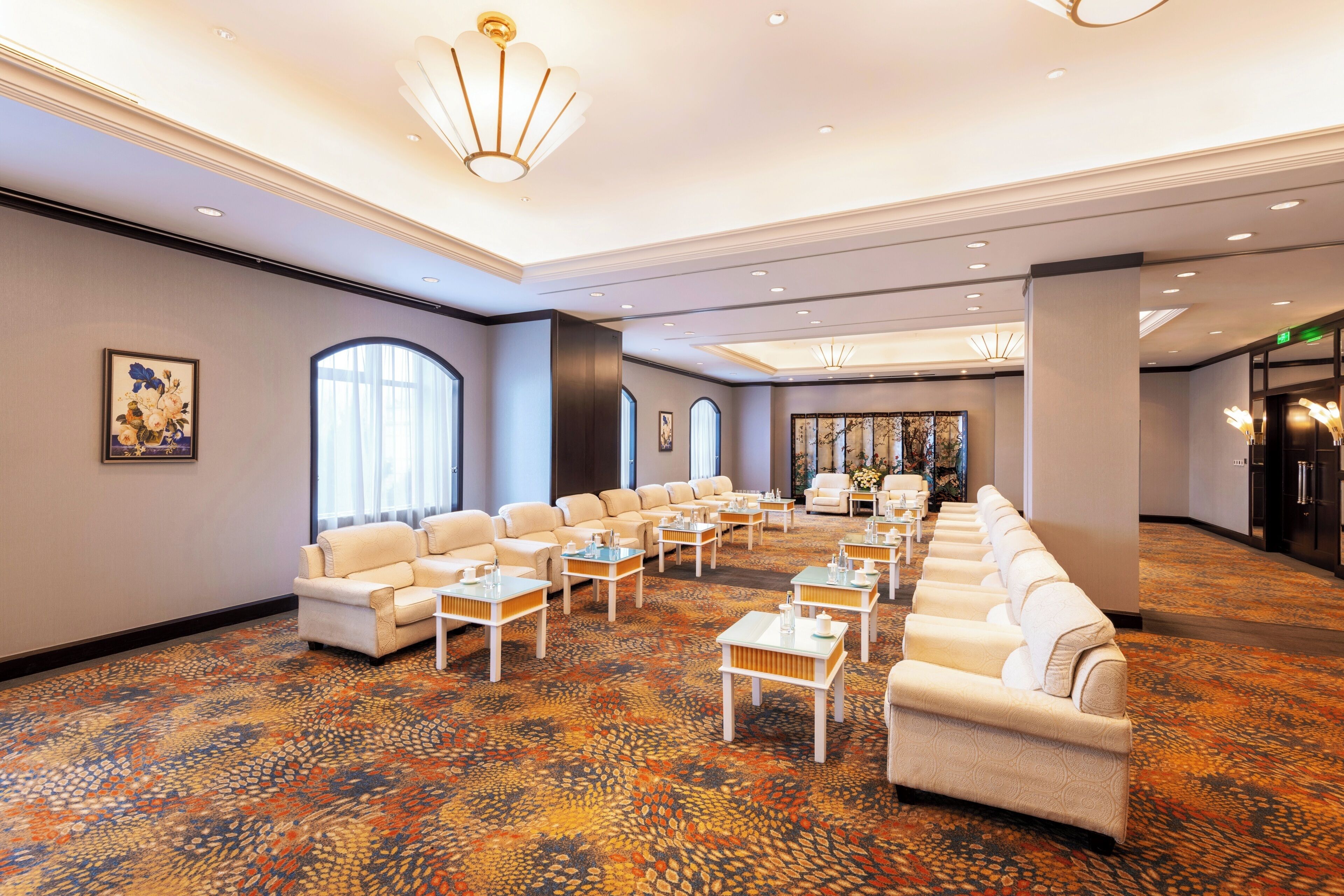 A spacious hotel lobby with multiple seating areas, a patterned carpet, and a modern chandelier.