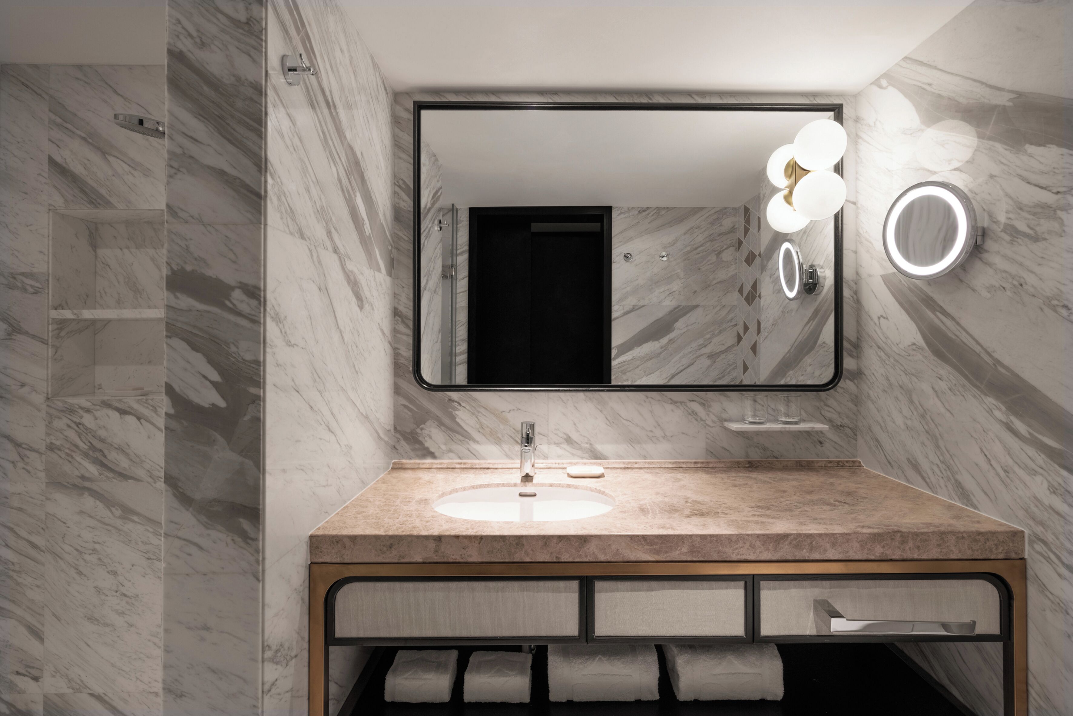 A modern bathroom with a marble wall, a wooden vanity, a sink, a mirror, and a towel rack.