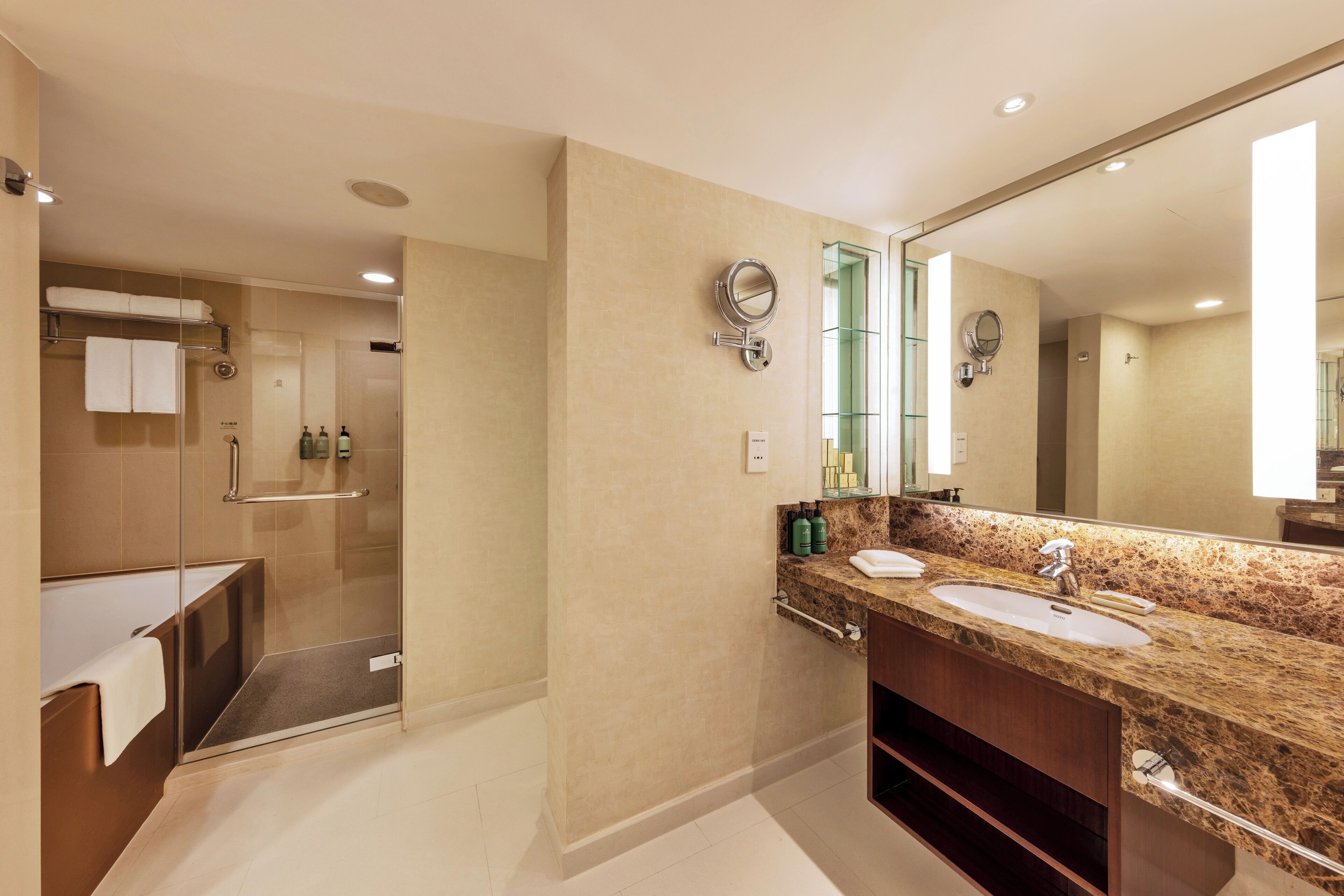 Un baño moderno con un espejo grande, dos lavamanos, una ducha y una ducha a ras de suelo con mampara de vidrio.