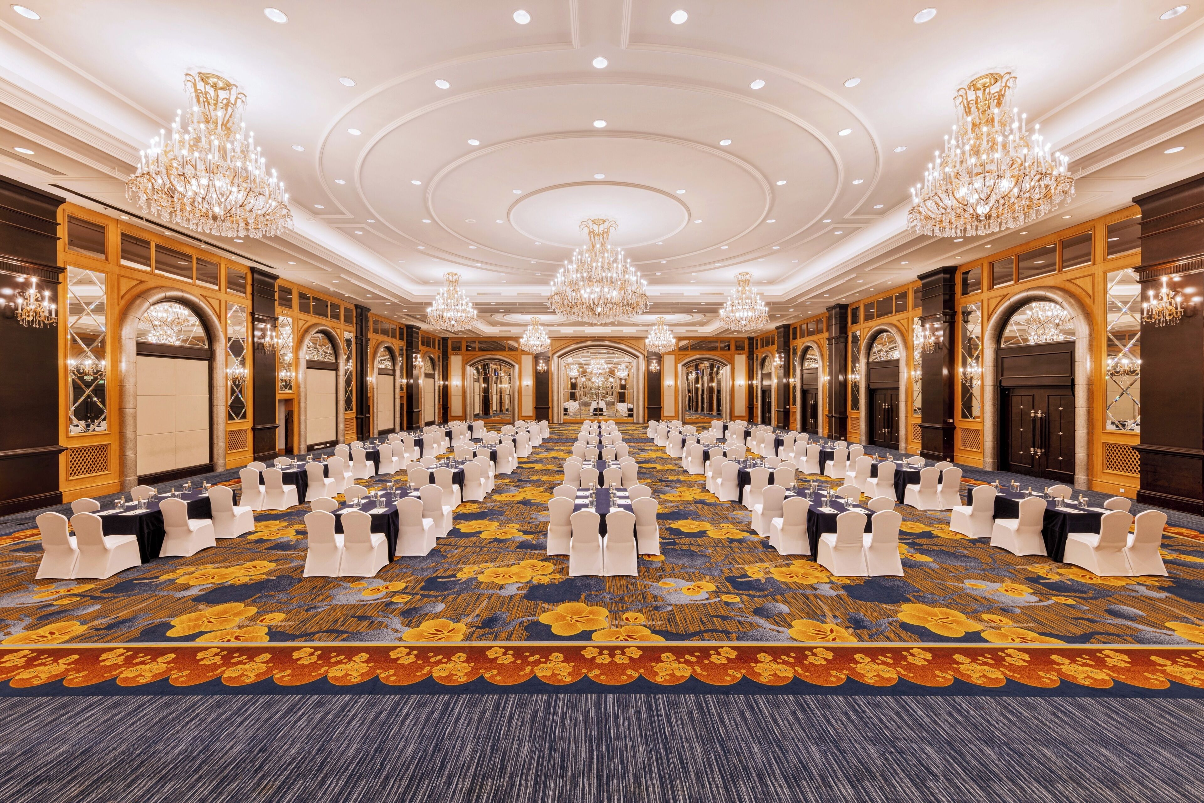 A large conference room with rows of tables and chairs, chandeliers, and ornate wooden paneling.