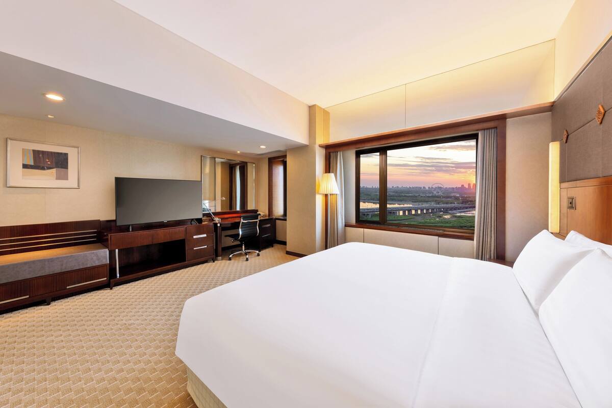 Una habitación de hotel con una cama grande, un escritorio, un televisor y una ventana con vista a la ciudad.