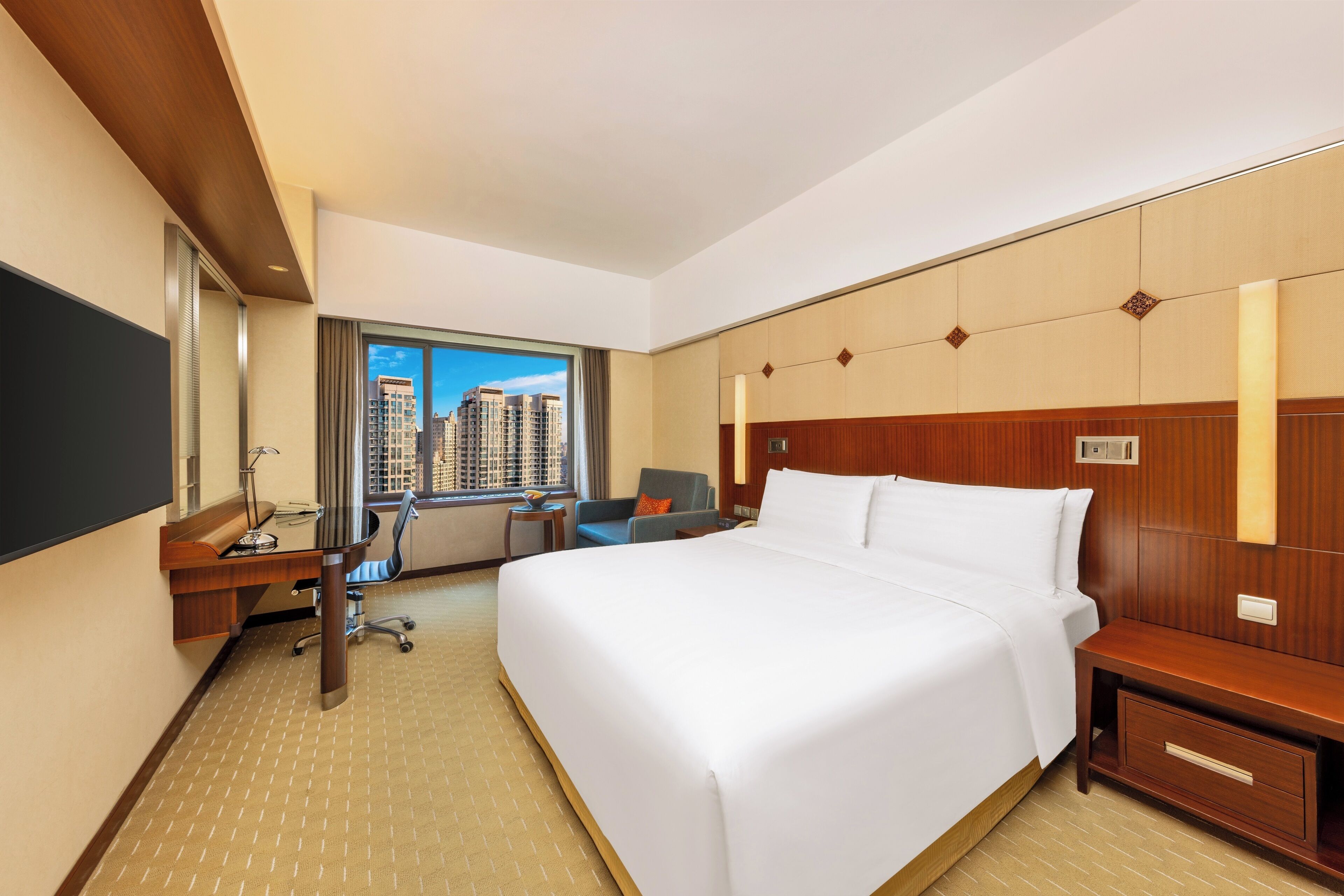 A hotel room with a large bed, a desk, a chair, a TV, and a window with a city view.