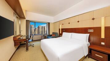 A hotel room with a large bed, a desk, a chair, a TV, and a window with a city view.