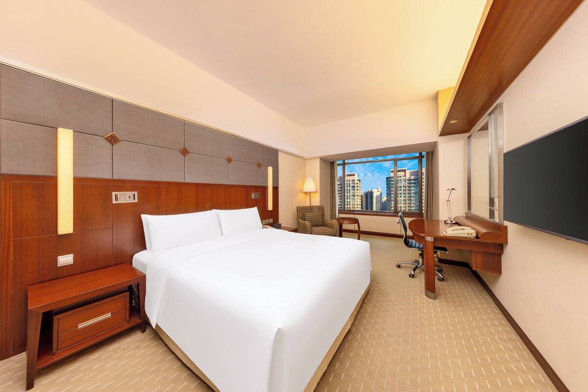 Habitación de hotel con una cama grande, un escritorio con una silla, una mesita y vistas a la ciudad.