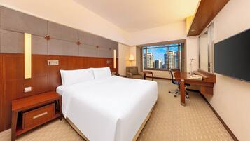 A hotel room with a large bed, a desk with a chair, a small table, and a view of the cityscape.