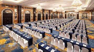 A large conference room with rows of tables and chairs, chandeliers, and ornate wooden doors.