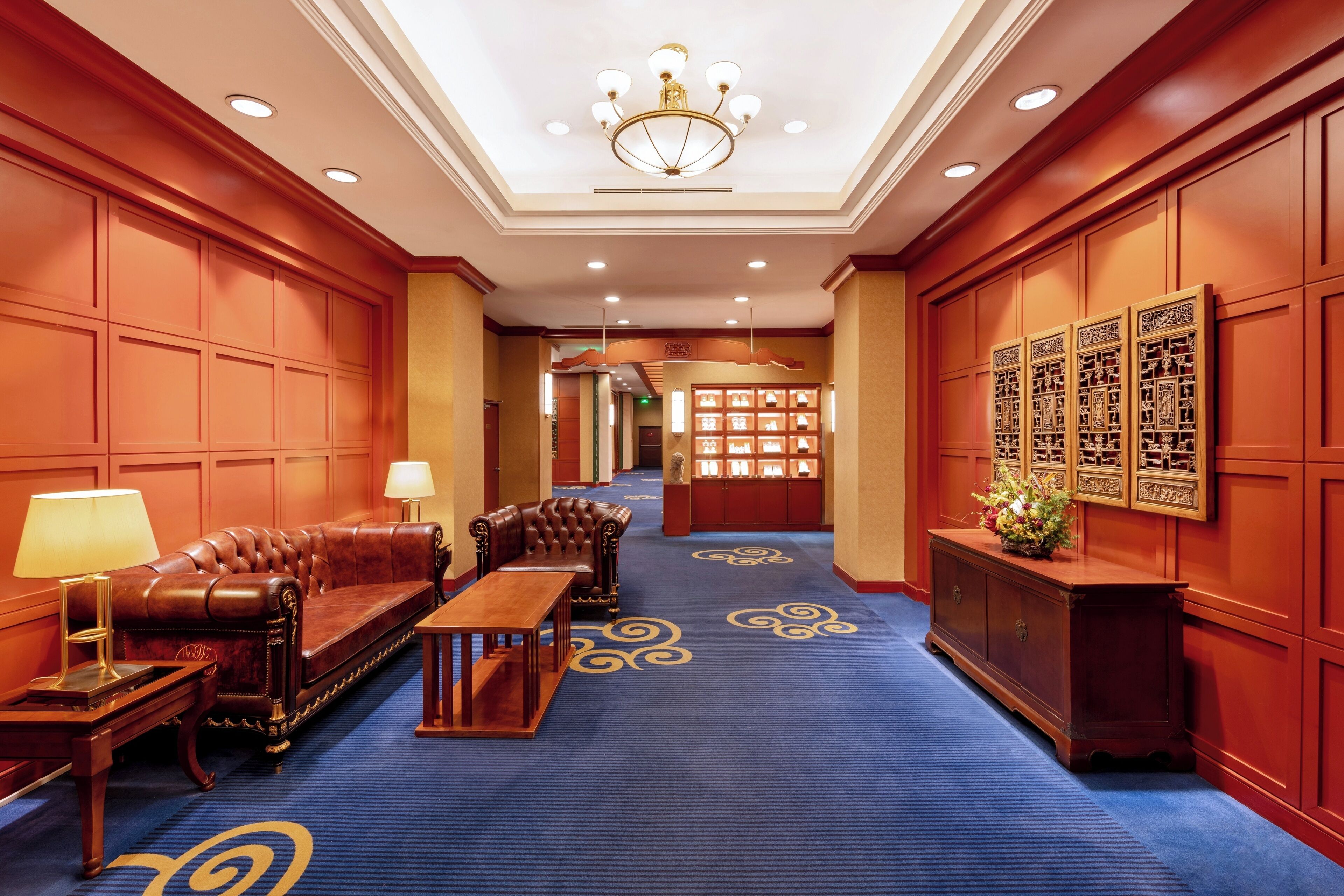 A hotel lobby with a blue carpet, leather sofa, wooden coffee table, and a chandelier.