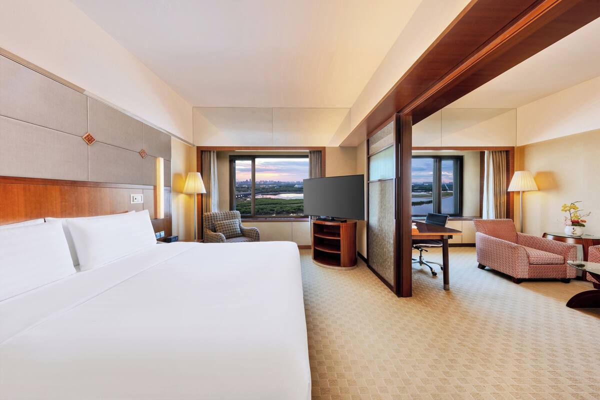 Habitación de hotel con una cama grande, un escritorio con silla, un televisor y vistas a la ciudad a través de la ventana.