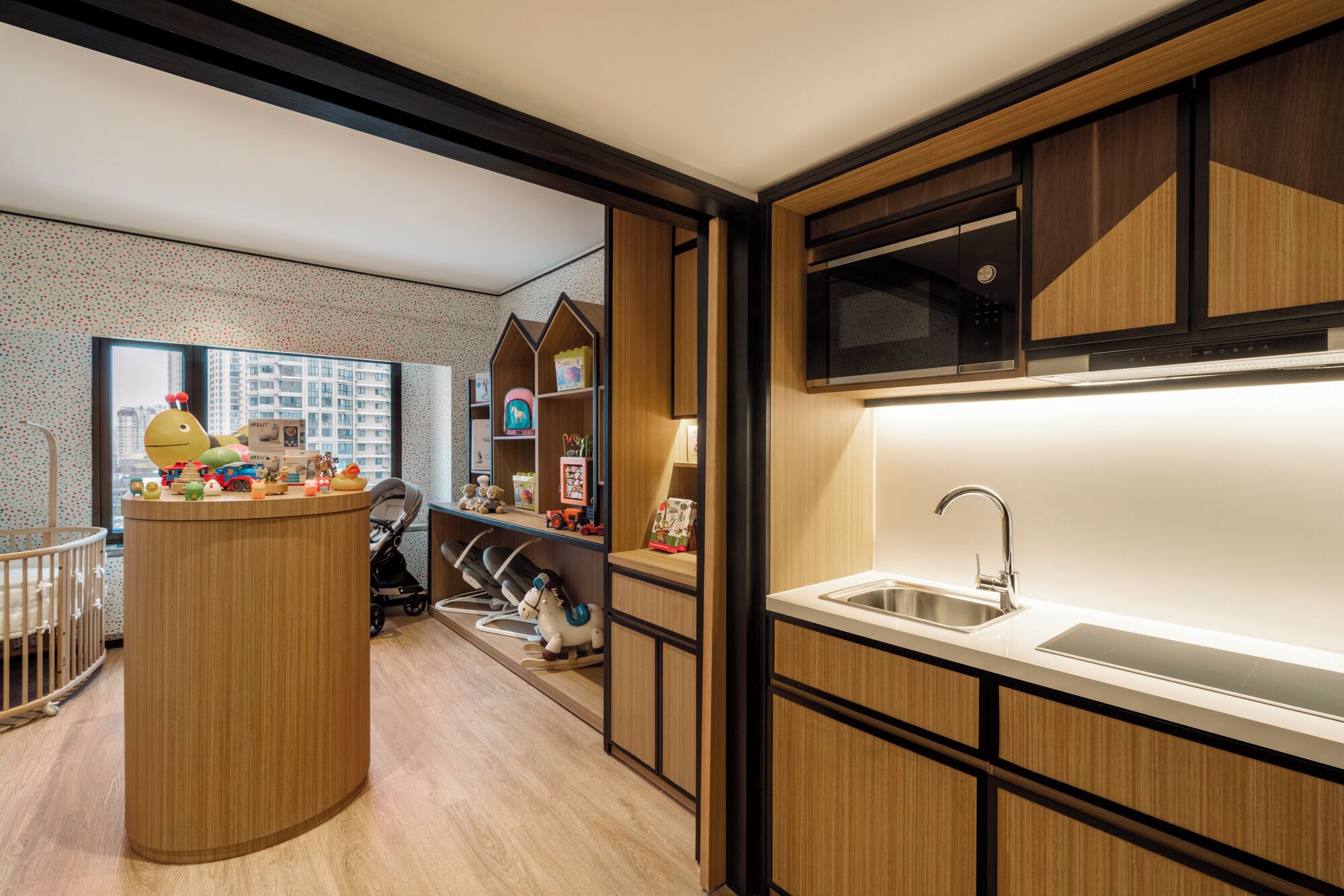 Una cocina moderna con microondas integrado, un fregadero y una zona de juegos de madera con juguetes y un cochecito.