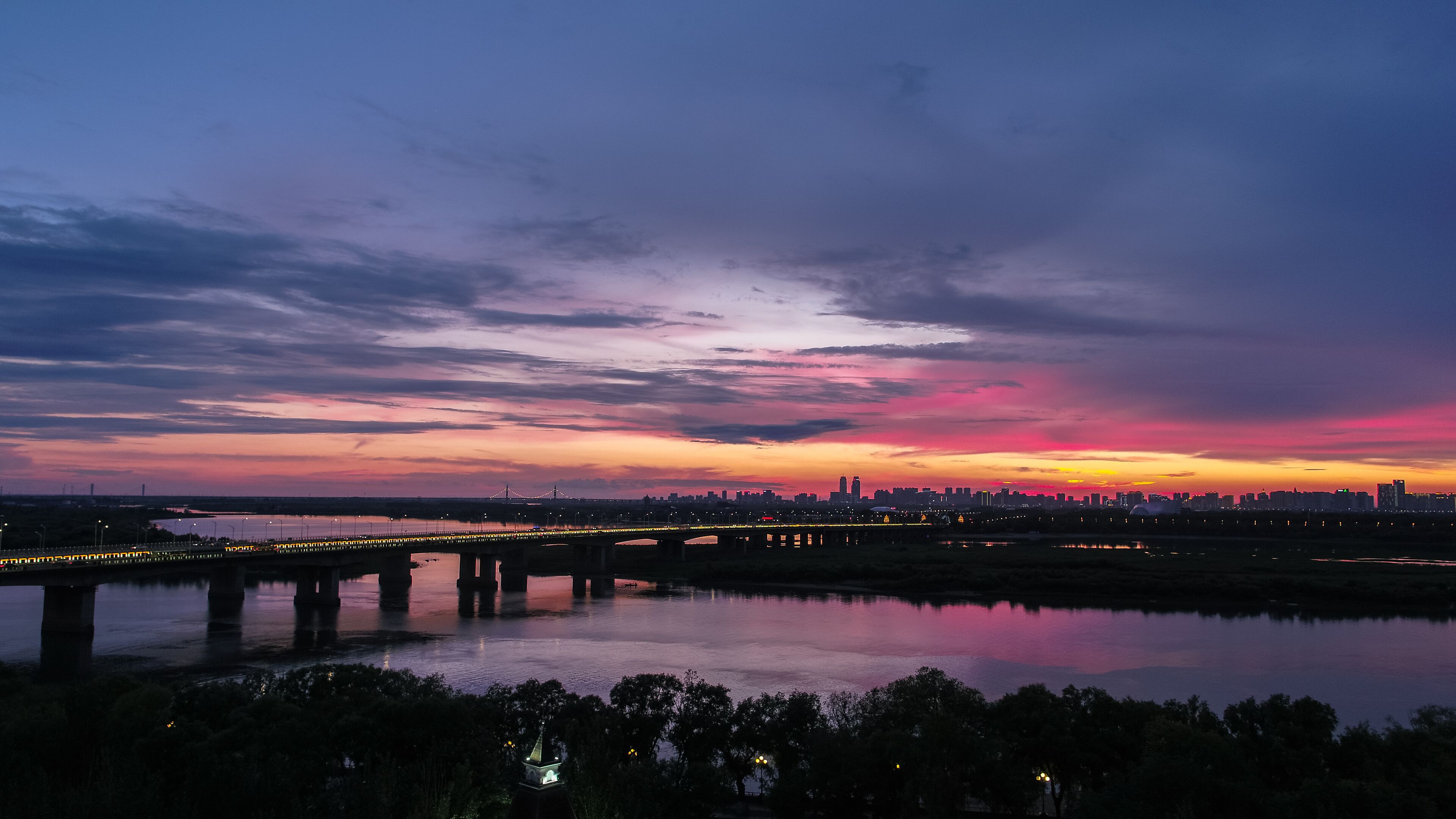 Atardecer sobre el horizonte de una ciudad con un puente cruzando un cuerpo de agua.