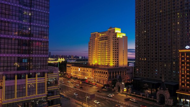 A high-rise hotel with a prominent 'Shangri-La' sign, surrounded by other tall buildings and a busy street below. - Shangri-La Harbin (Harbin)