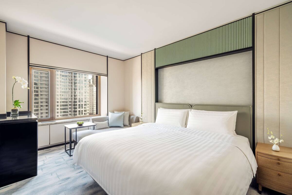 Una habitación de hotel moderna con una cama grande, un escritorio pequeño, una silla y una ventana con vistas a la ciudad.