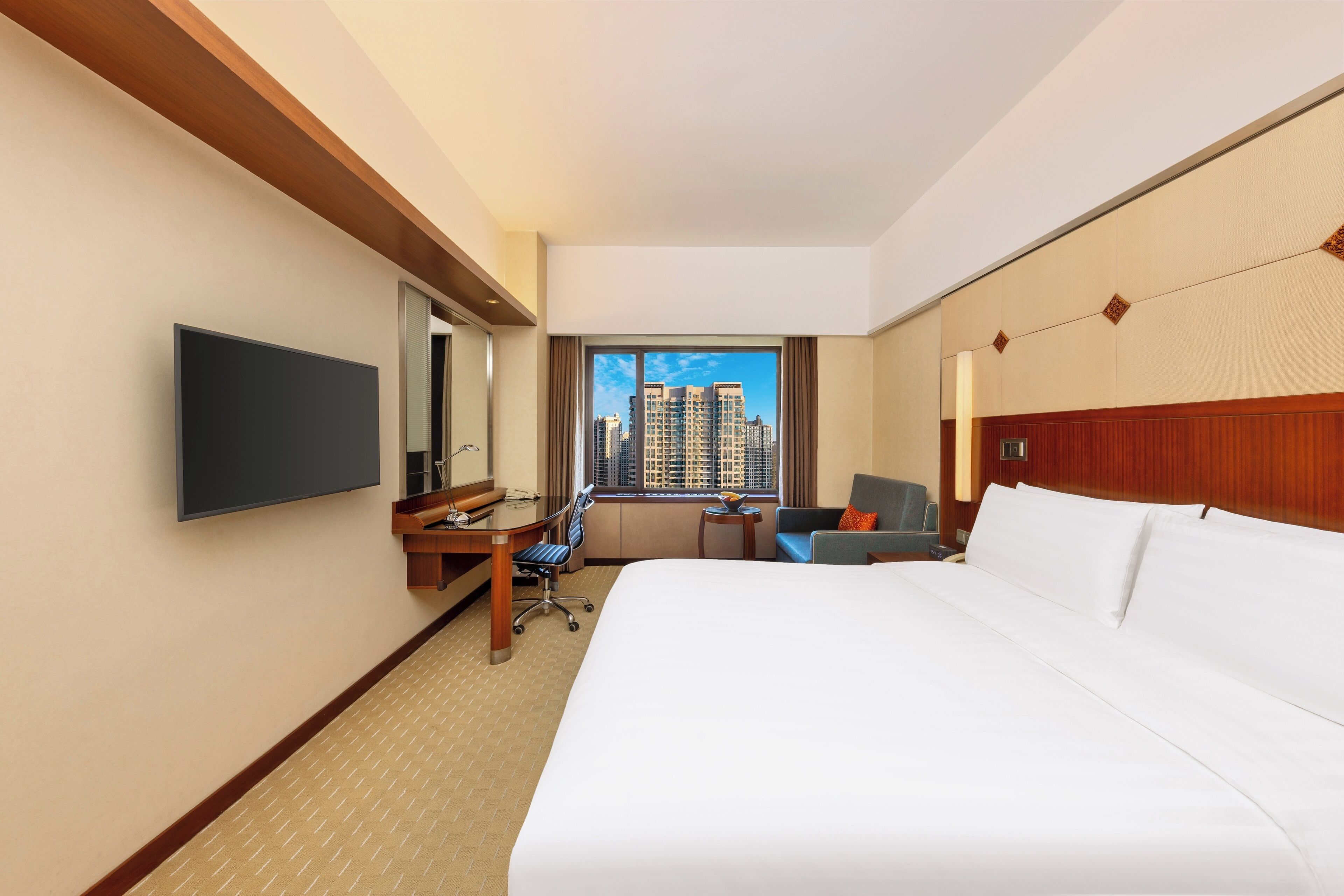 A hotel room with a large bed, a desk, a chair, a TV, and a window with a city view.