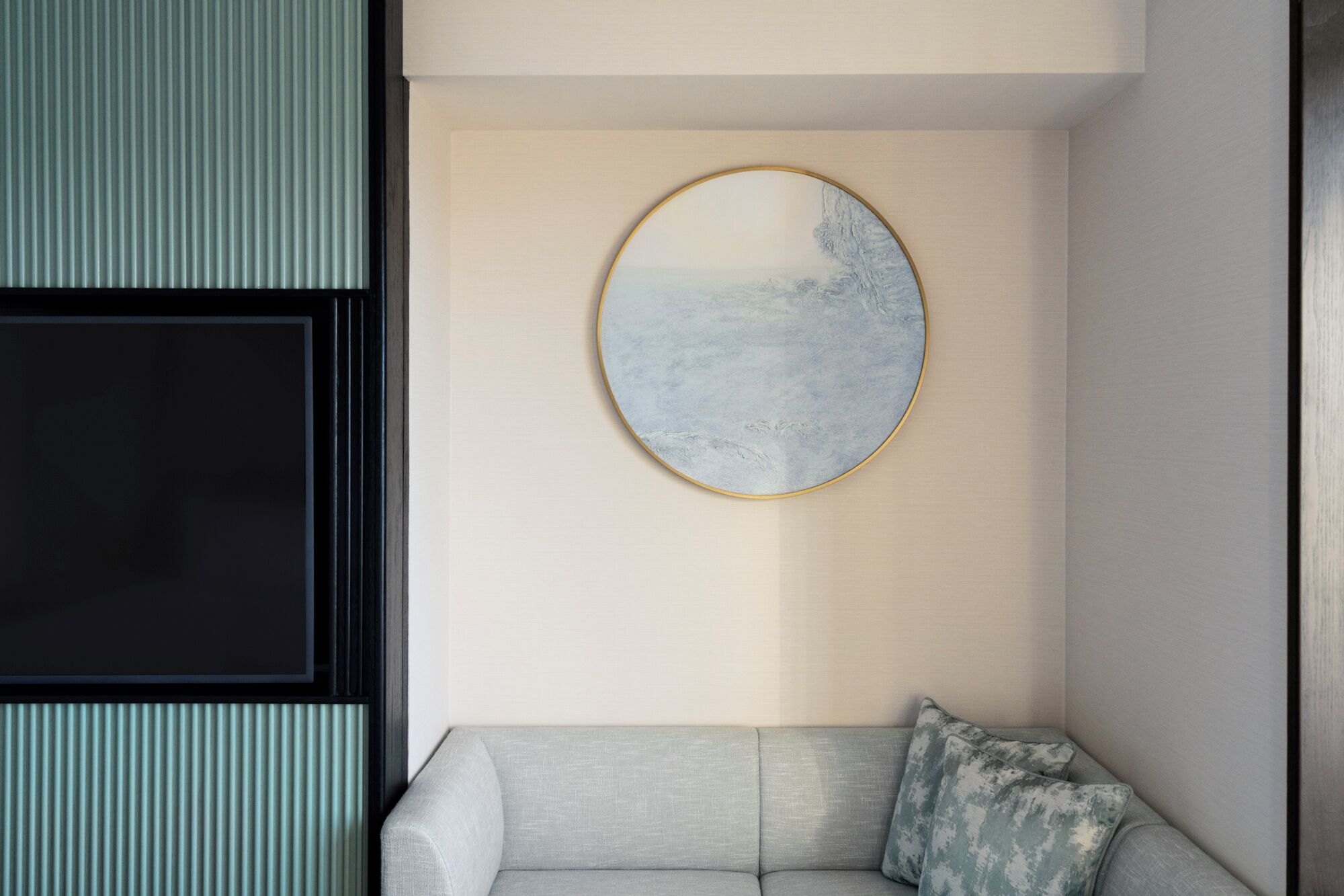 A room with a light grey sofa, a round mirror with a gold frame, and a textured wall.