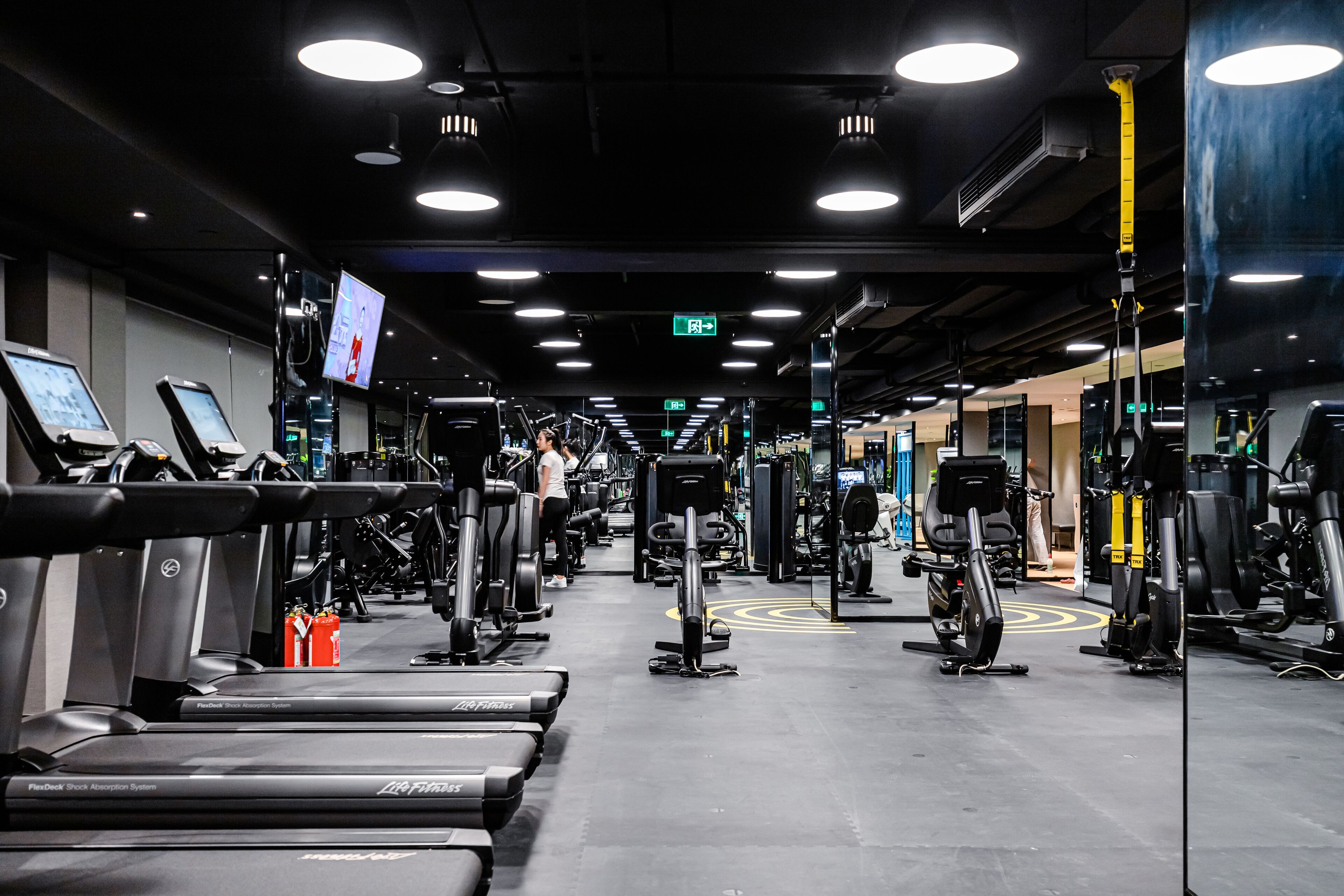 Ein Fitnessstudio mit Laufbändern, Kraftgeräten und einem Spiegel.