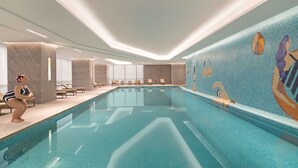 A modern indoor swimming pool with a clear view of the pool area, lounge chairs, and a mural on the wall.