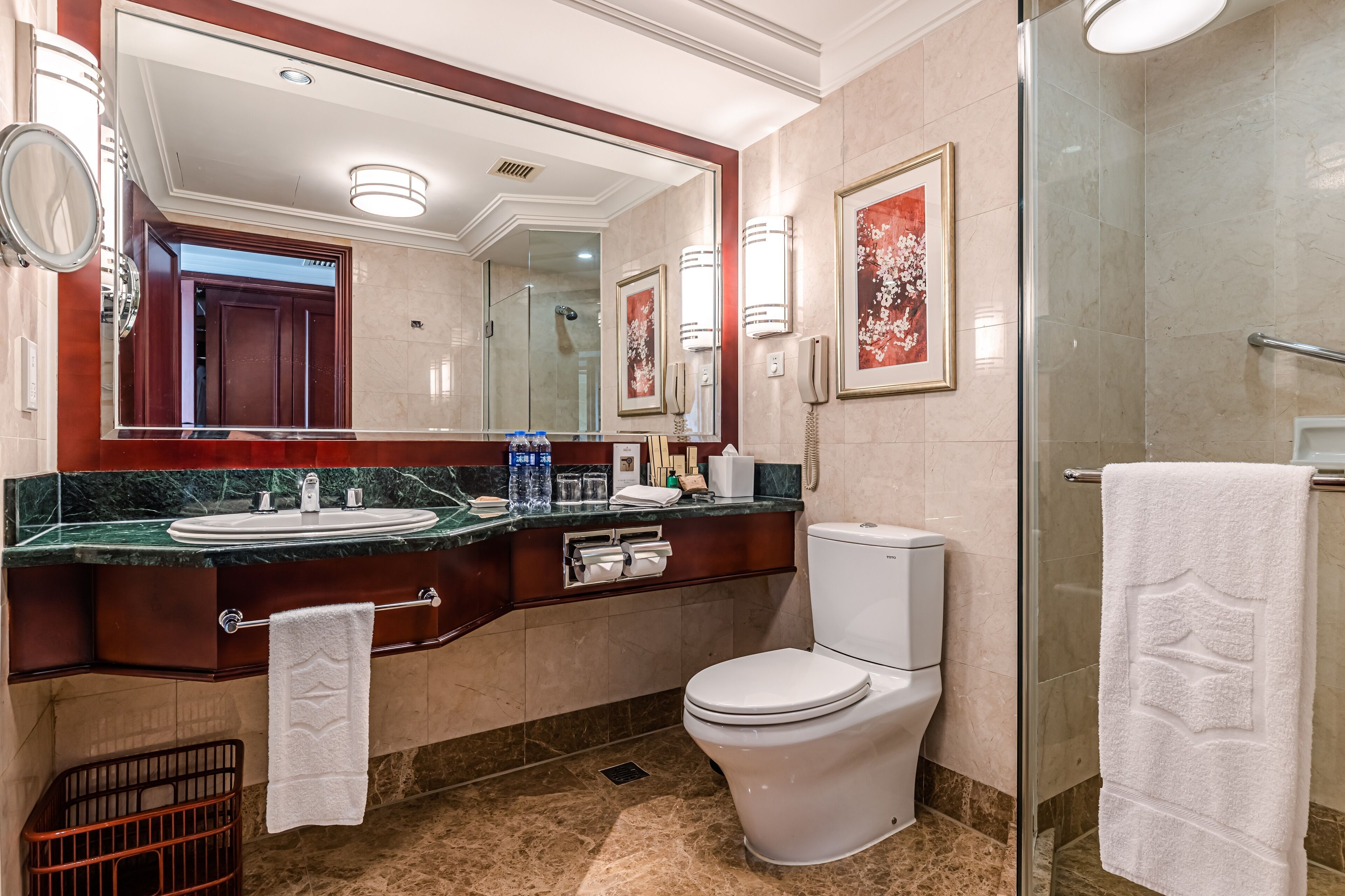 A modern bathroom with a large mirror, marble countertop, white toilet, and a glass shower enclosure.