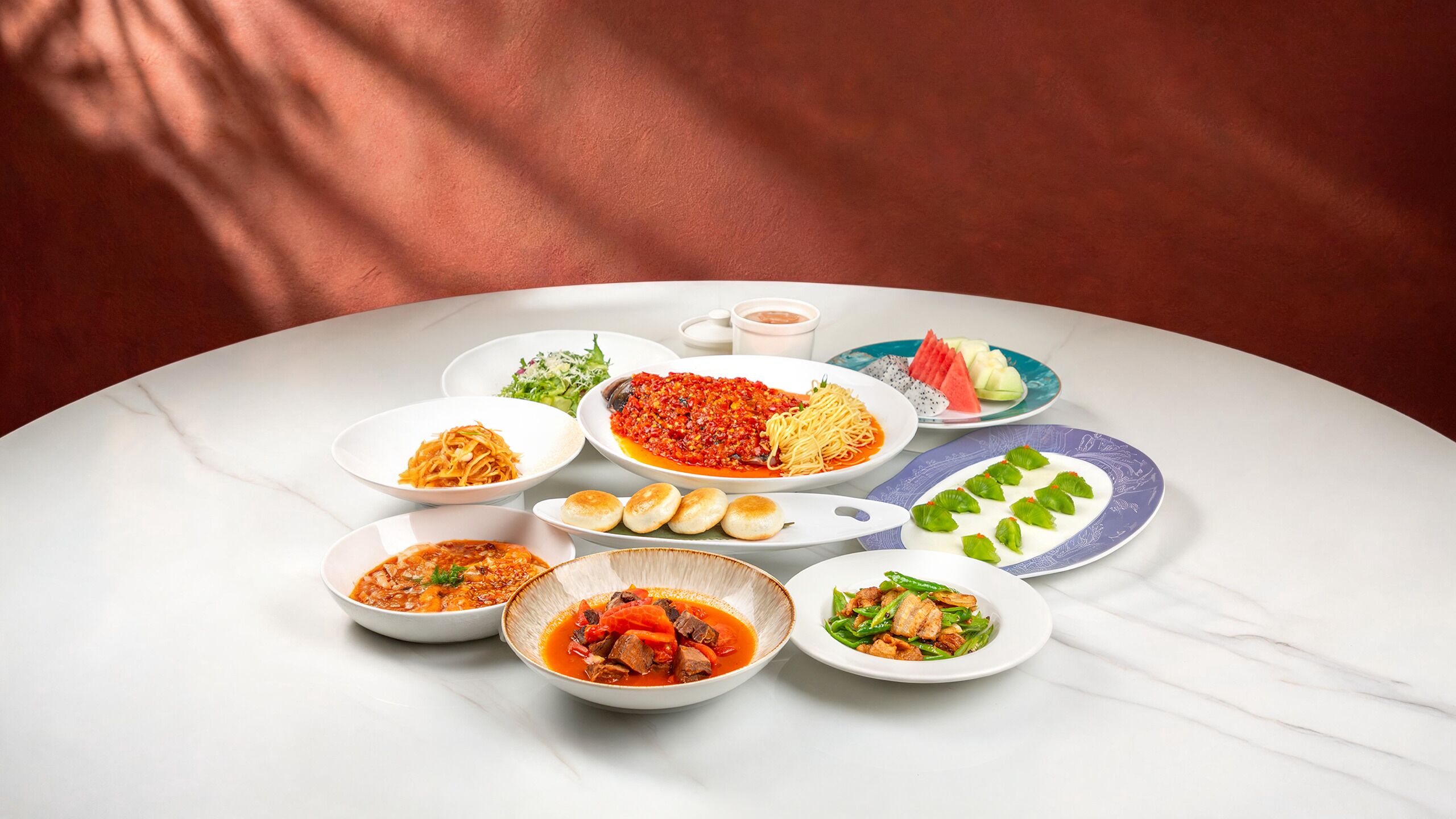 A variety of dishes on a marble table against a red background.