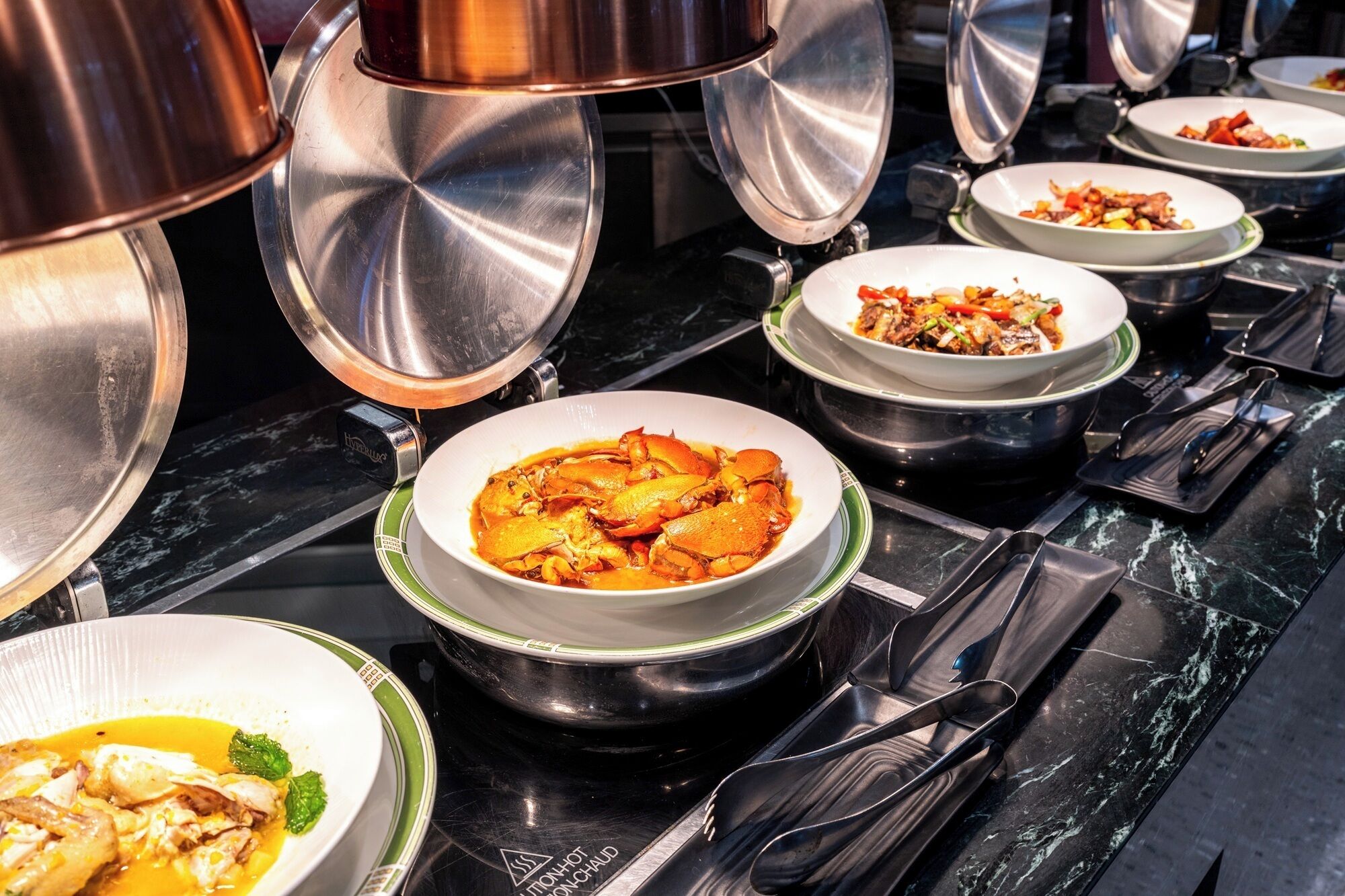 A buffet setup with various dishes in bowls on a black marble countertop.