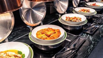 A buffet setup with various dishes in bowls on a black marble countertop.