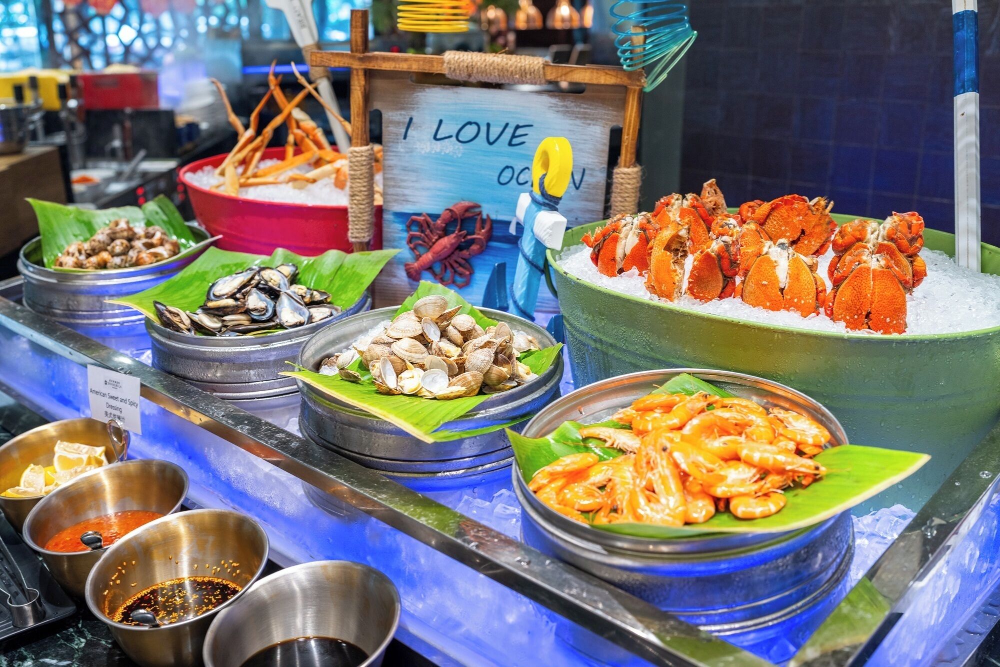 A seafood display with various types of shellfish and shrimp, including oysters, clams, and prawns, arranged on ice and garnished with leaves.