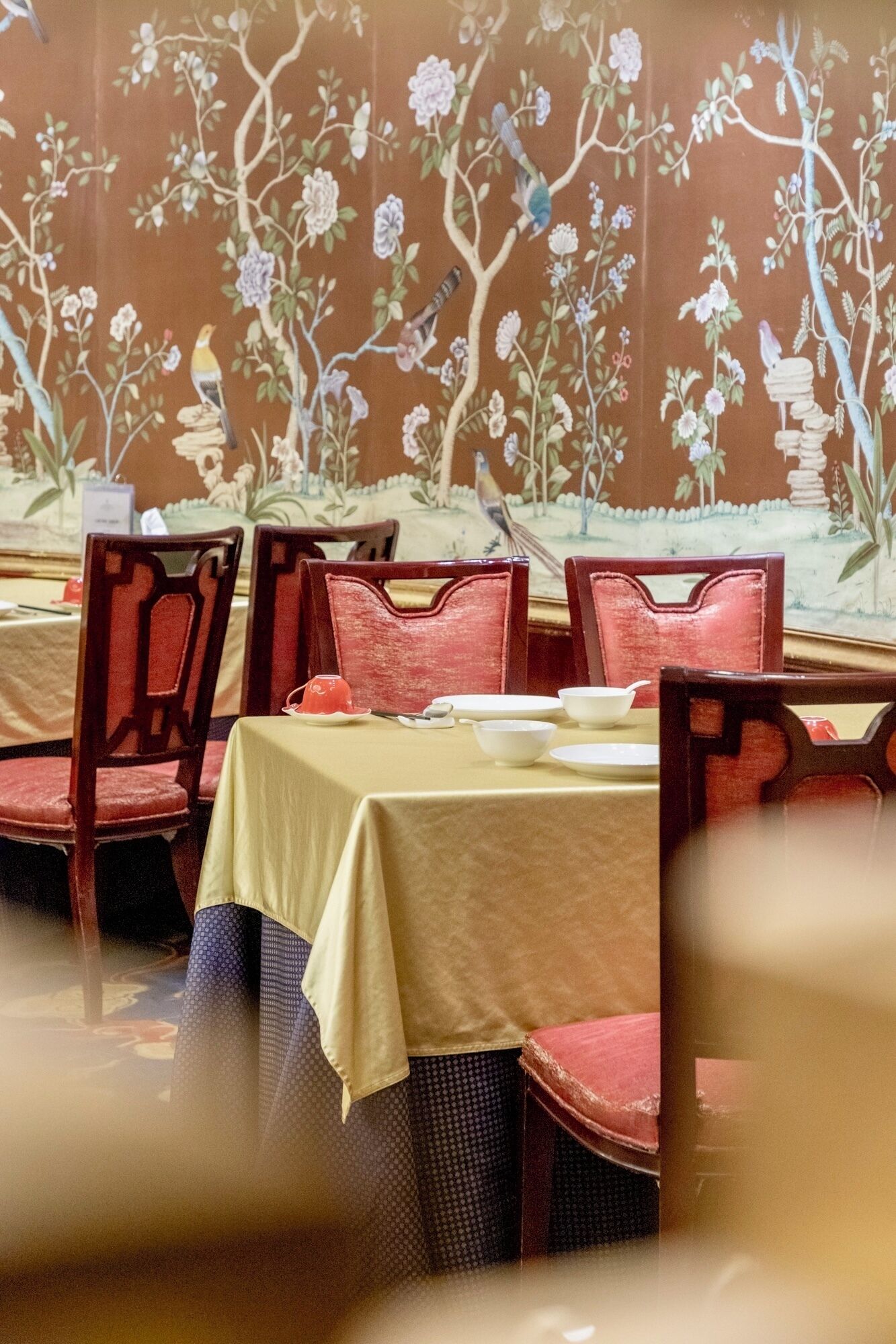 Un comedor con mesas y sillas, un mural floral en la pared y un suelo estampado.