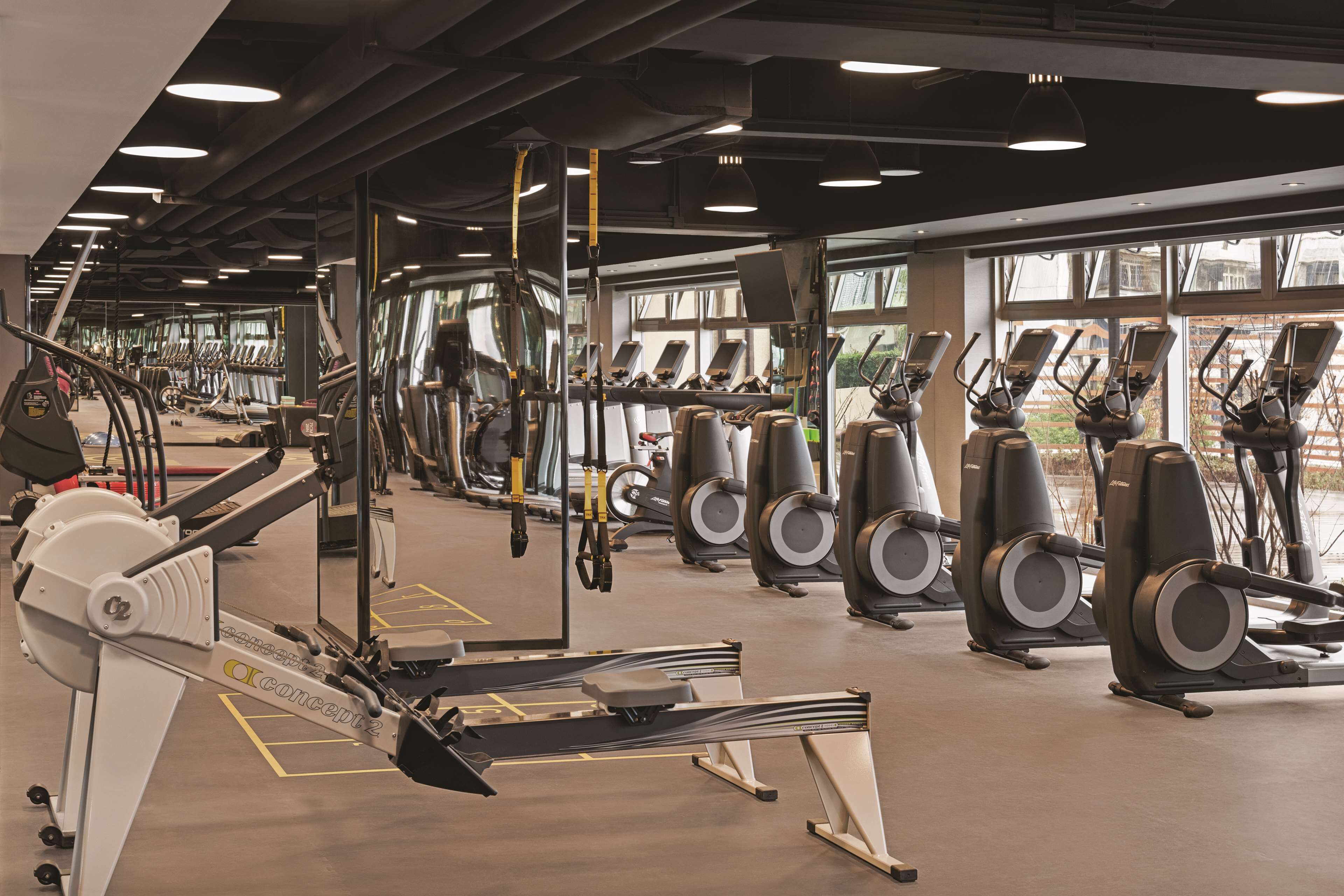 A gym with various exercise machines, large windows, and a modern design.