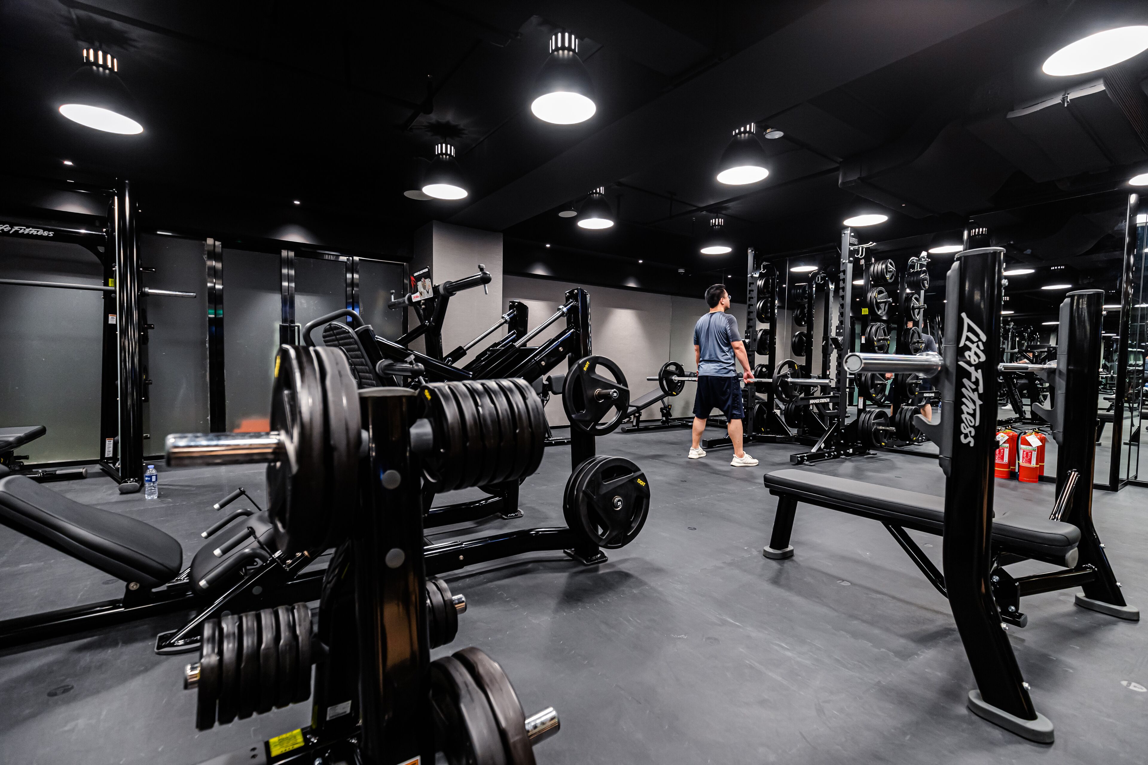 A gym with various weightlifting equipment and a person exercising.
