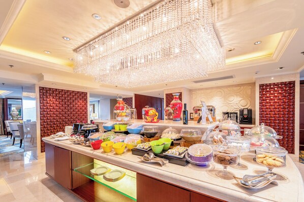 A buffet with various food items, a chandelier, and a red textured wall.