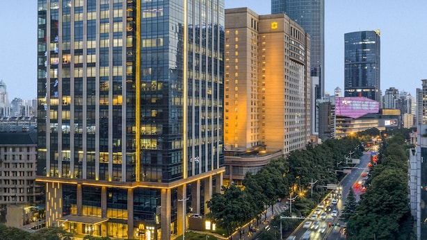 A modern high-rise building with a glass facade and illuminated signage.