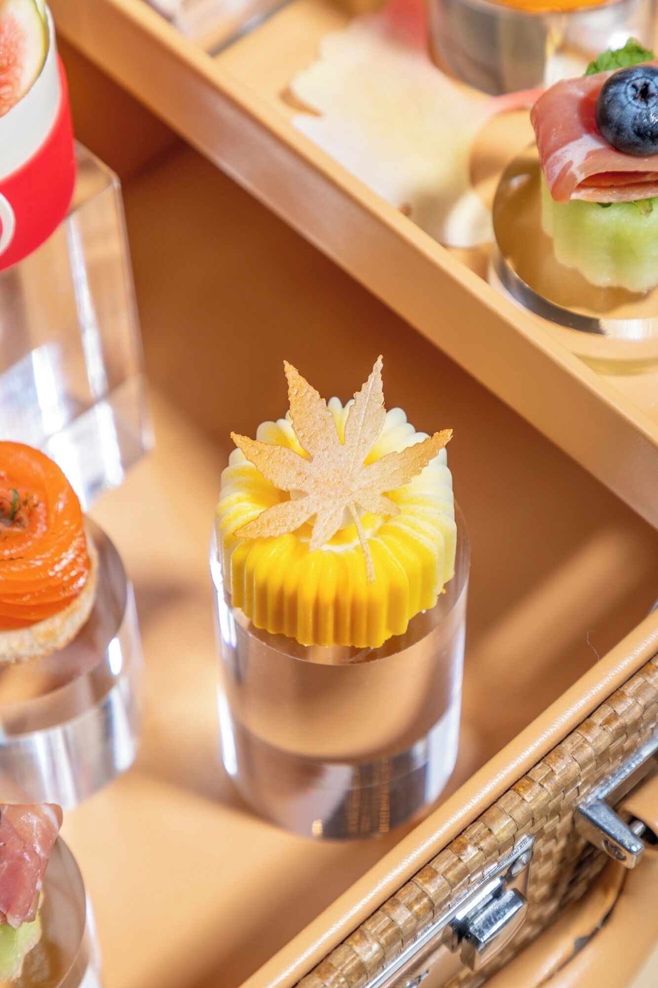 A dessert tray with various small dishes, including a yellow dessert with a leaf garnish.