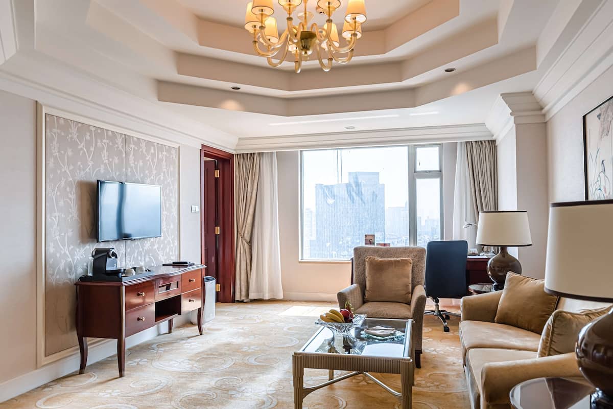 A spacious living room with a flat-screen TV, a wooden desk, a comfortable sofa, and a glass coffee table.