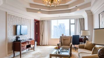 A spacious living room with a flat-screen TV, a wooden desk, a comfortable sofa, and a glass coffee table.