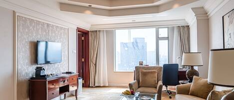 A spacious living room with a flat-screen TV, a wooden desk, a comfortable sofa, and a glass coffee table.