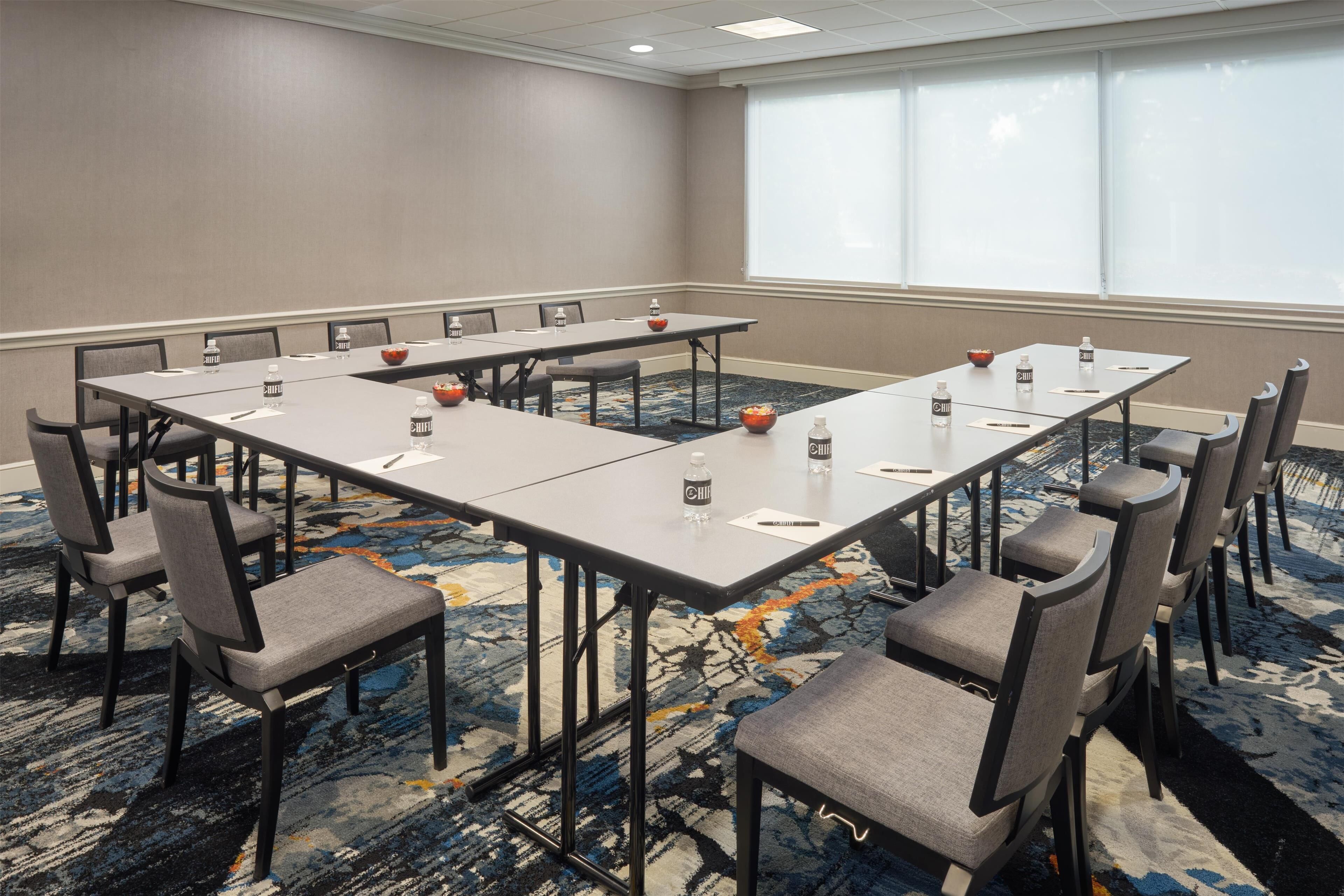 A conference room with a long table, chairs, water bottles, and a bowl of fruit.