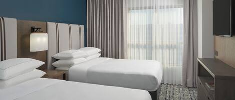 Habitación de hotel con dos camas, televisor, escritorio y ventana con cortinas.