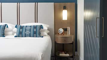 Een net opgemaakt bed met opvallende kussens, een nachtkastje met een klok en een wandlamp.