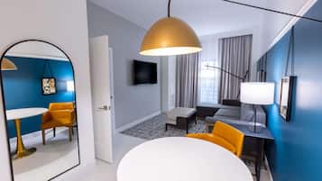 Une chambre d’hôtel moderne dotée d’un grand miroir, d’une table de salle à manger ronde, d’un canapé et d’un téléviseur fixé au mur.