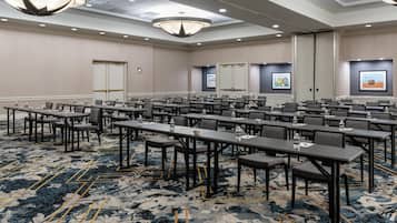 A conference room with multiple tables and chairs, a patterned carpet, and a modern chandelier.